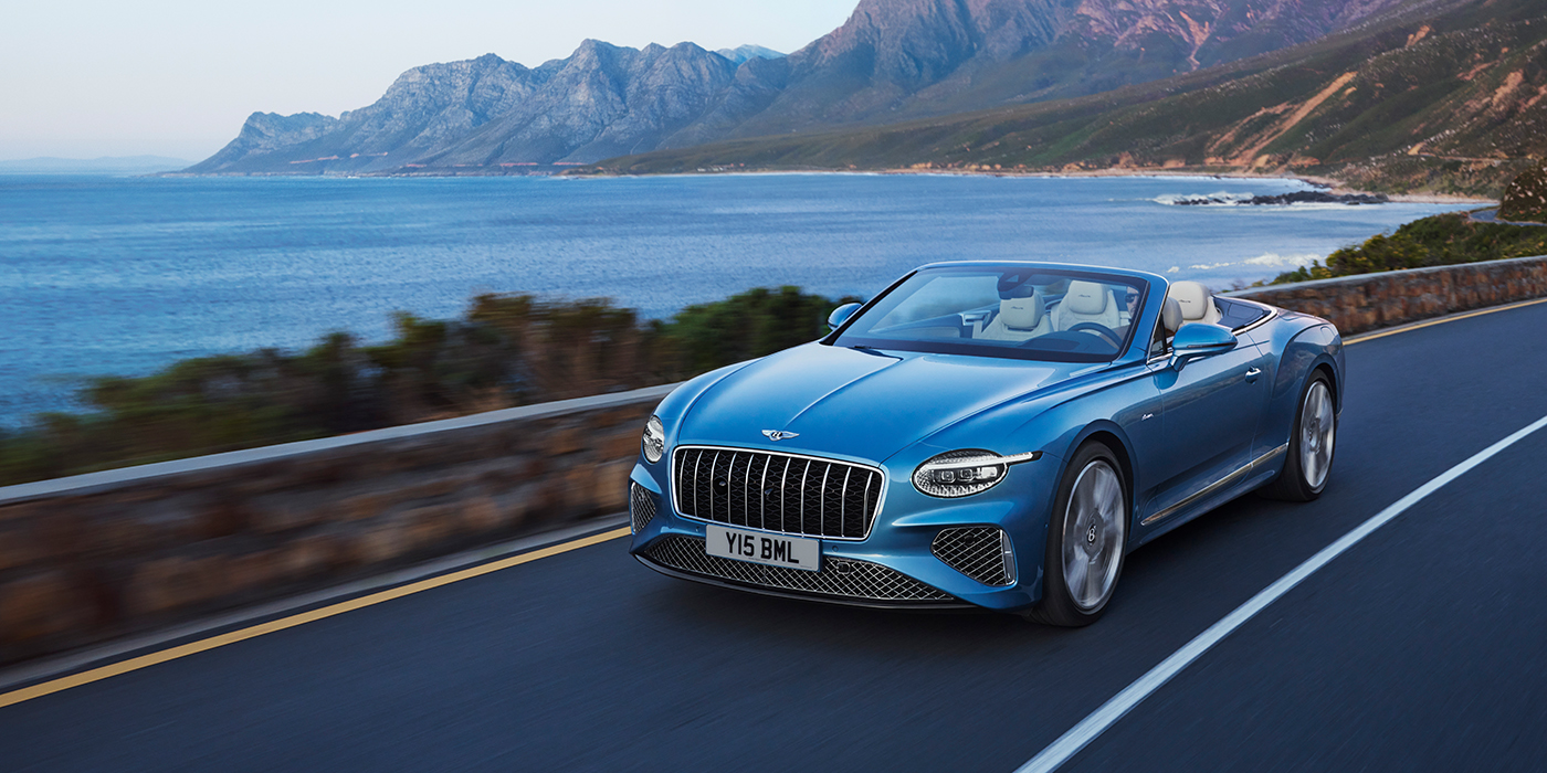 Bentley San Juan New Bentley Continental GTC Azure convertible in Light Windsor blue paint with 22 inch Azure wheels and chrome grill, driving dynamically by the sea