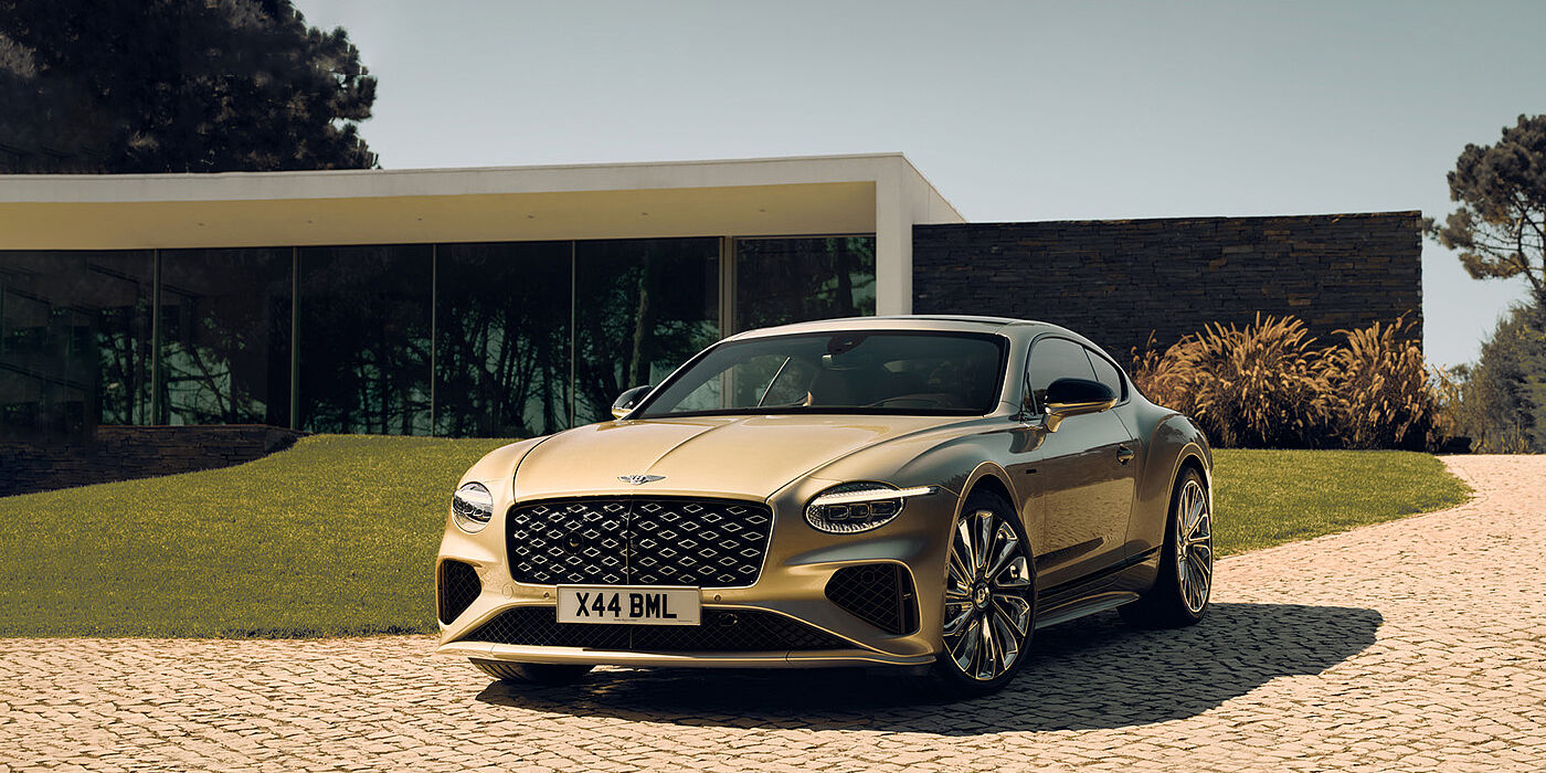 Bentley San Juan Bentley Continental GT Mulliner coupe front three quarters in Patina paint parked outside a glass fronted building with a grass lawn behind it