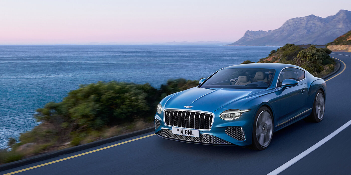 Bentley San Juan New Bentley Continental GT Azure coupe in Light Windsor blue paint with 22 inch Azure wheels and chrome grill, driving dynamically by the sea