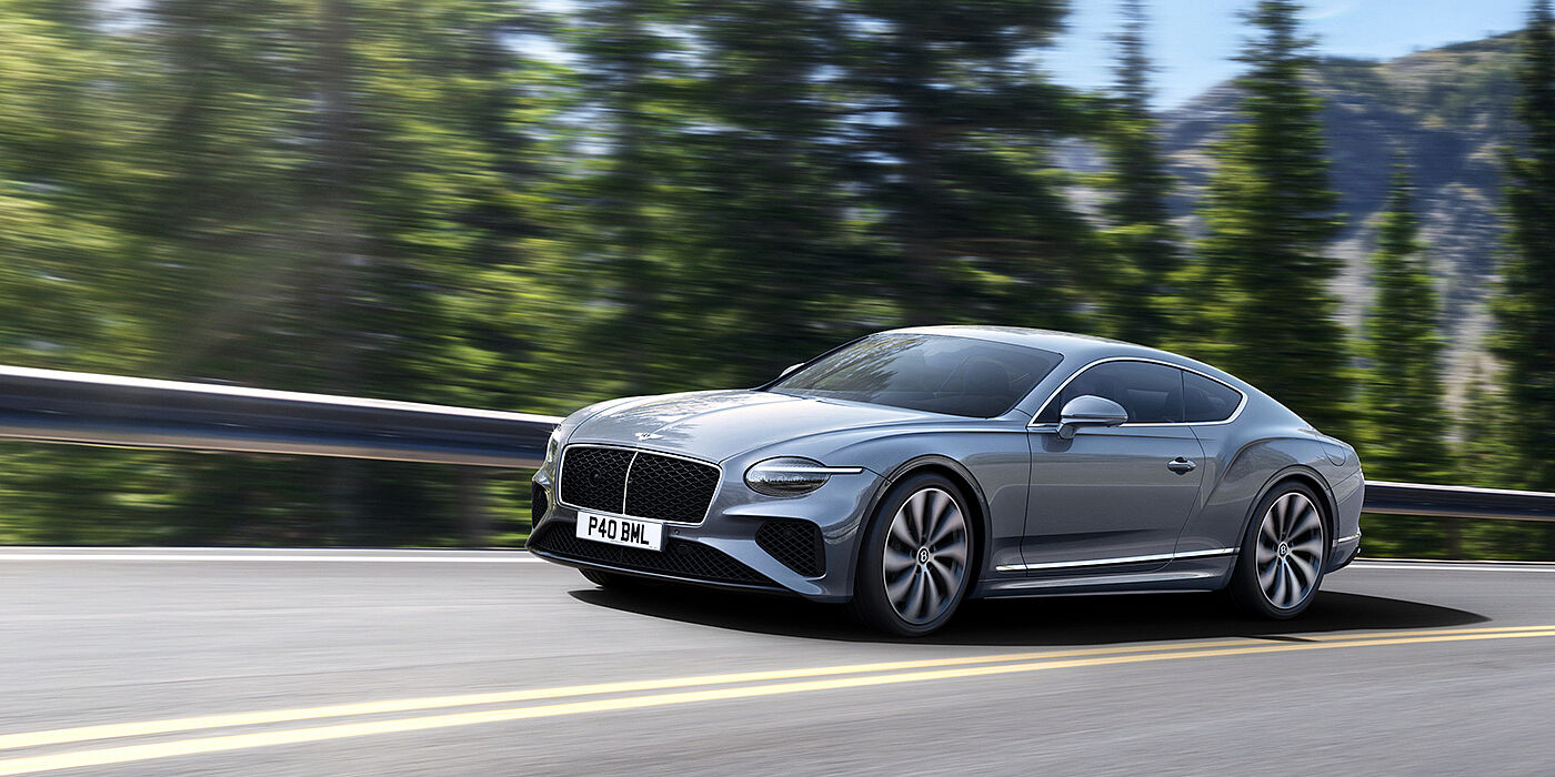 Bentley San Juan New Bentley Continental GT coupe in Silverlake paint and 22 inch ten-spoke wheels, driving dynamically on a tree-lined road in the sunshine