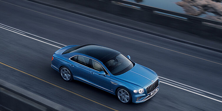 Bentley San Juan New Bentley Flying Spur Azure sedan in Light windsor blue paint by Mulliner, with 22 inch Azure wheels seen from overhead driving dynamically on a country road