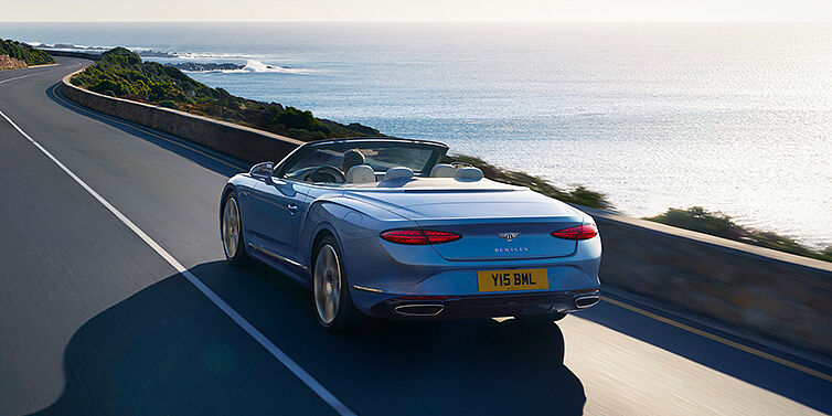 Bentley San Juan New Bentley Continental GTC Azure convertible rear view in Light Windsor blue paint with 22 inch ten spoke wheels driving dynamically on an ocean road in the sunshine
