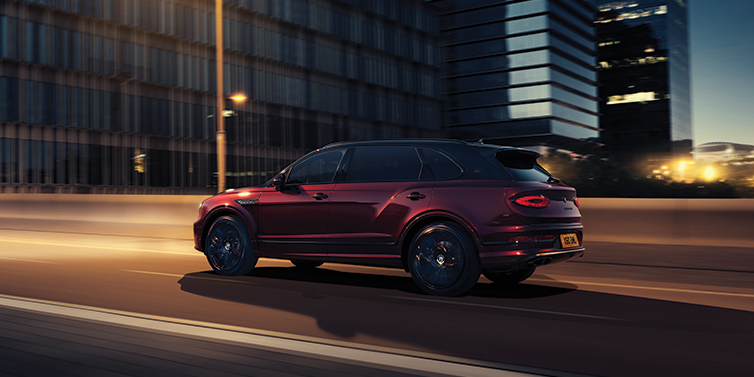 Bentley San Juan Bentley Bentayga Extended Wheelbase Mulliner SUV in Cricket Ball red paint driving dynamically in city at night